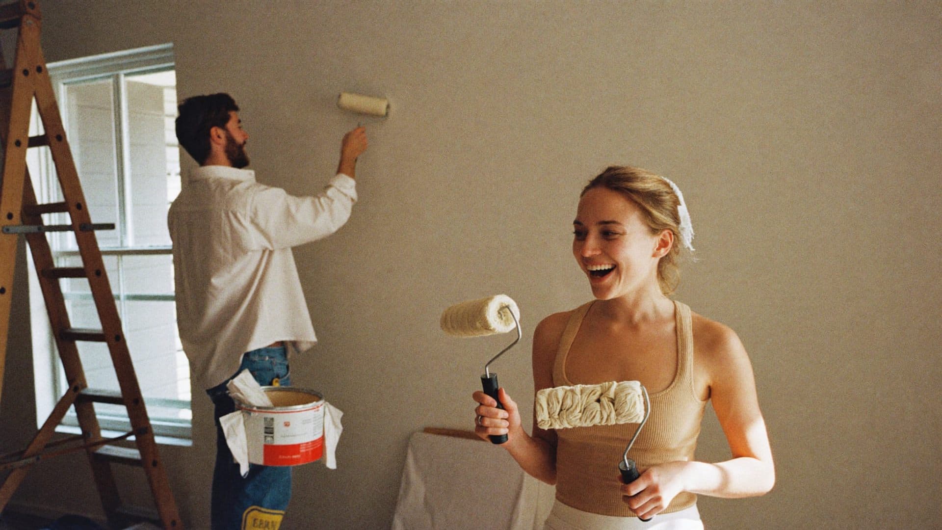 A couple painting the wall of their first home, laughing